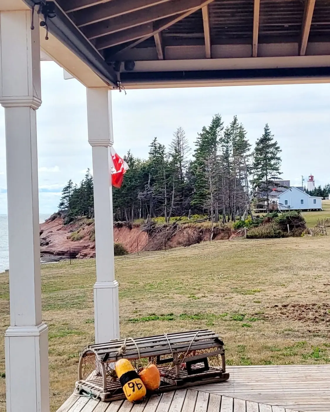 The covered porch of the Coastal Knook, with the flag, a lobster trap, and the red cliffs and lighthouse beyond