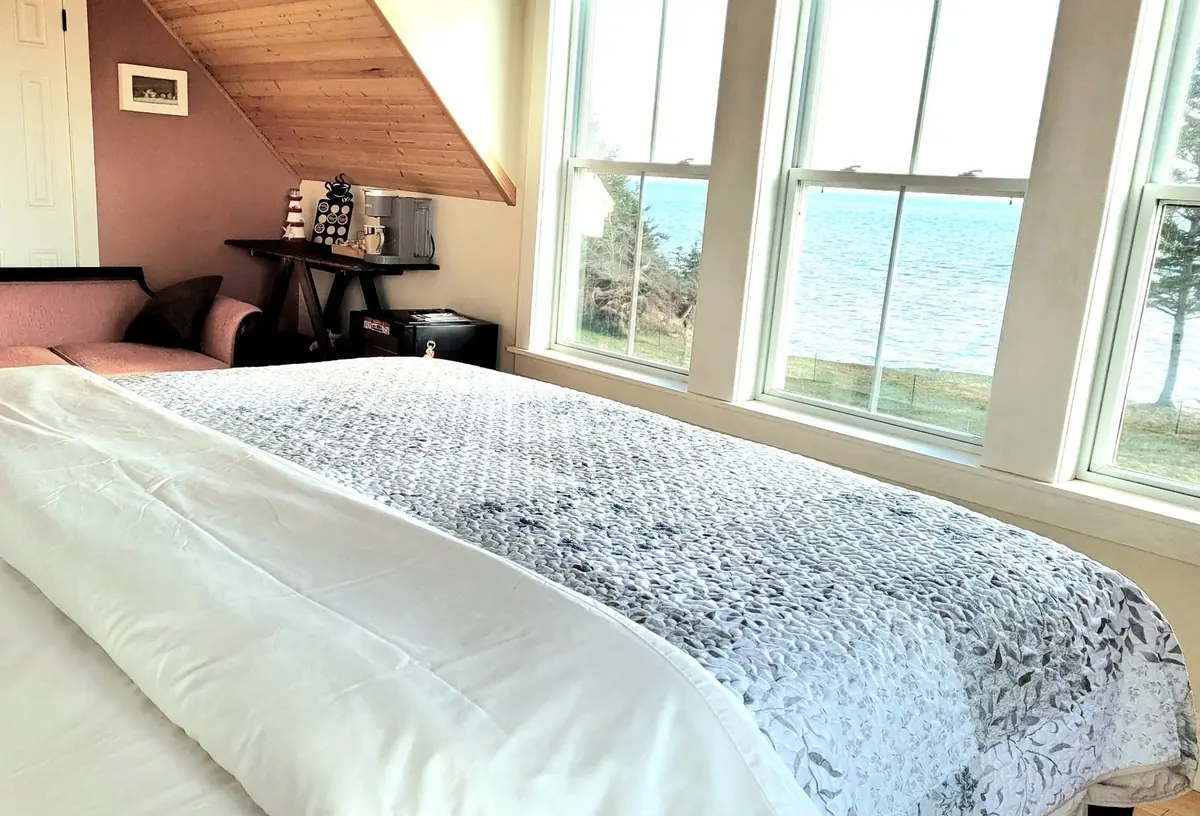 Guest bedroom with a white duvet and dormer windows looking out at the water