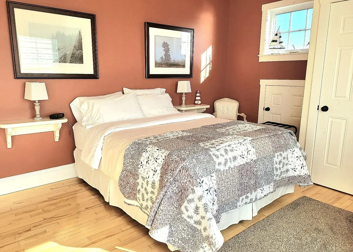 Guest bedroom with warm terracotta walls, framed art and a made bed